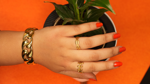 Hand with 18k gold plated jewelry on an orange background