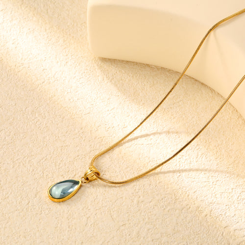 18k gold plated necklace with a teardrop-shaped pendant on a beige surface 18K Gold Plated on premium Stainless Steel, this necklace  is 100% waterproof, sweat-proof, and anti-tarnish. Designed for active women. Skin-friendly for the Chennai gym heat. Buy 2 Get 1 FREE!