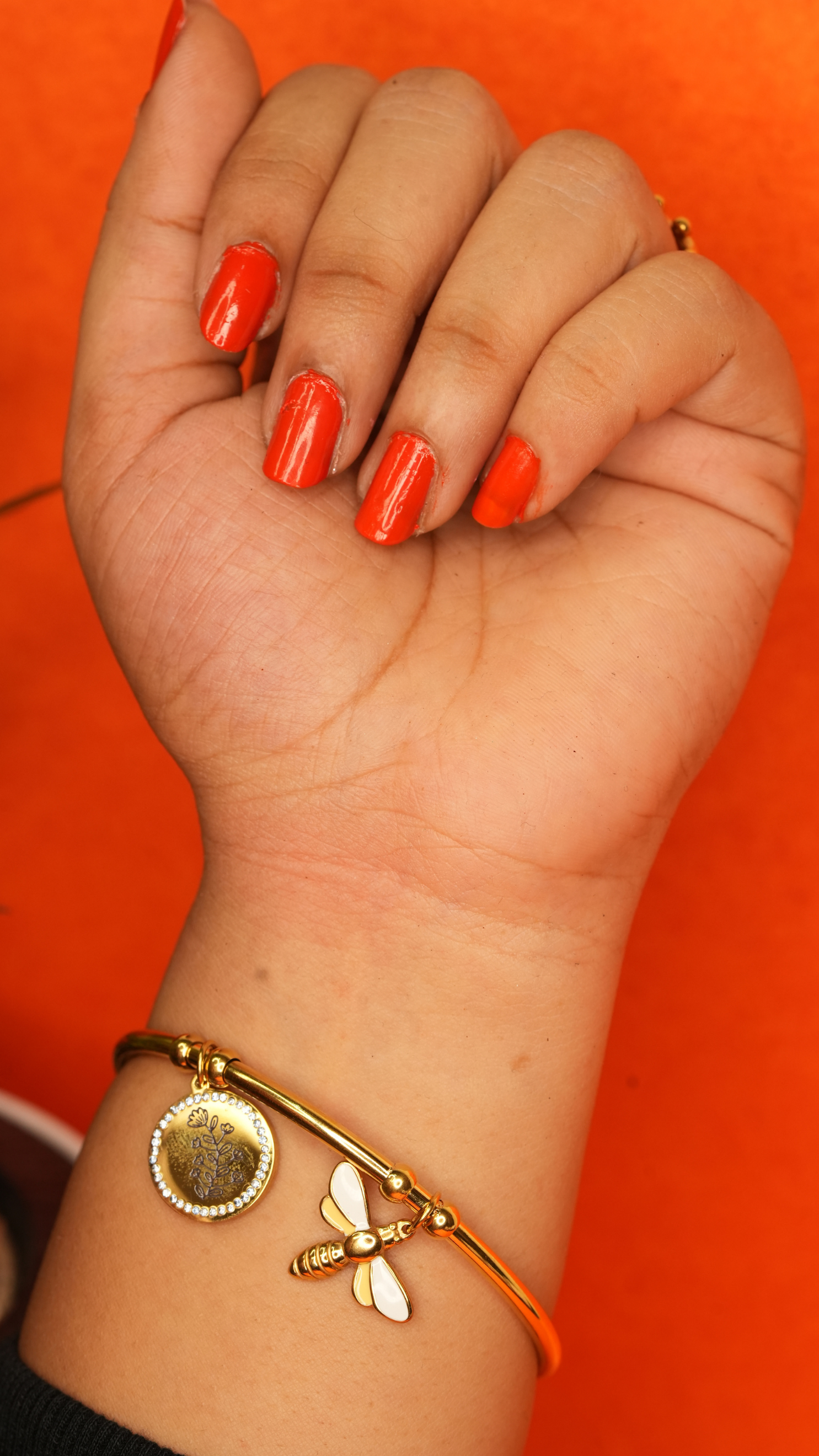 Hand with red nail polish and a gold bracelet on an orange background