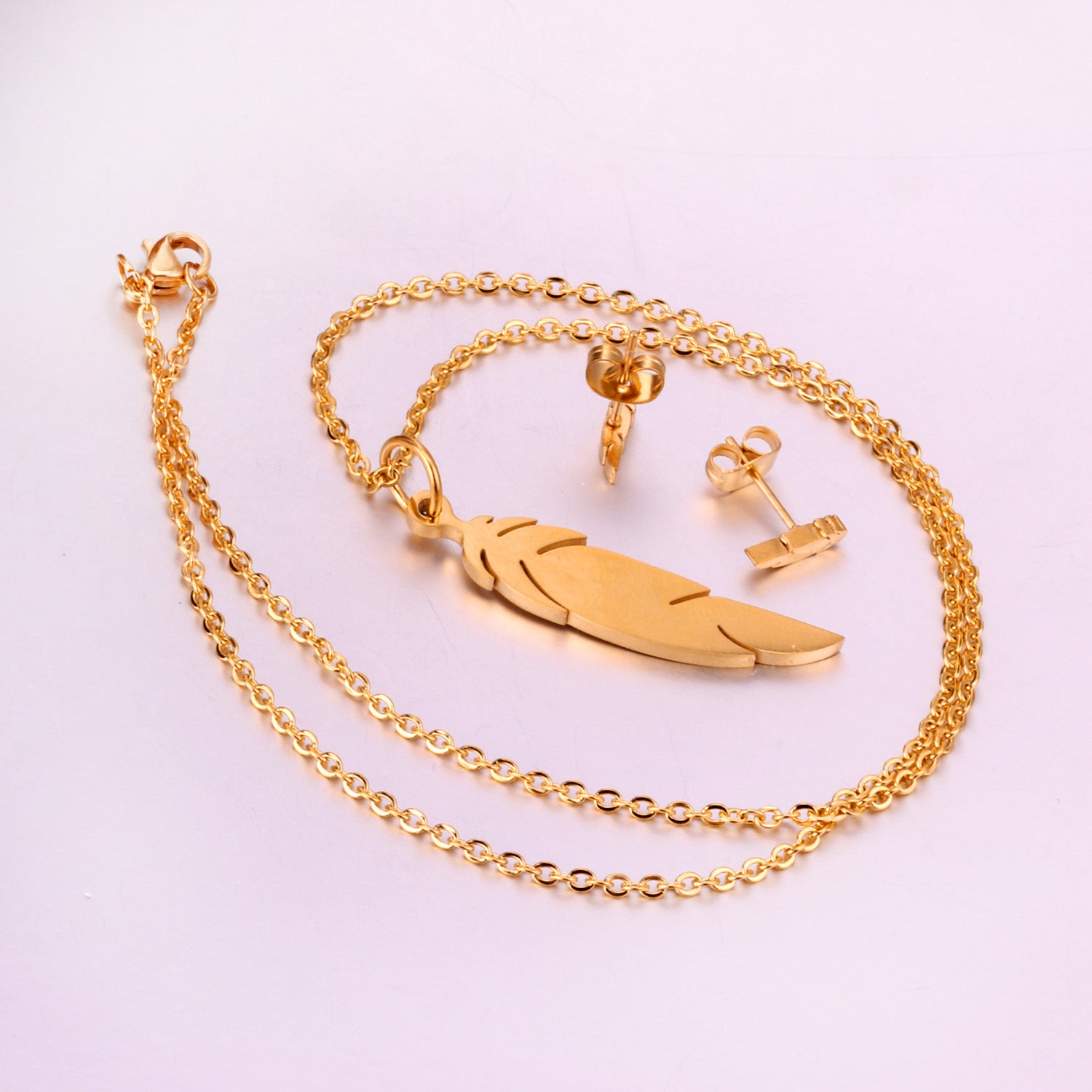 Gold necklace with feather pendant on a light pink background