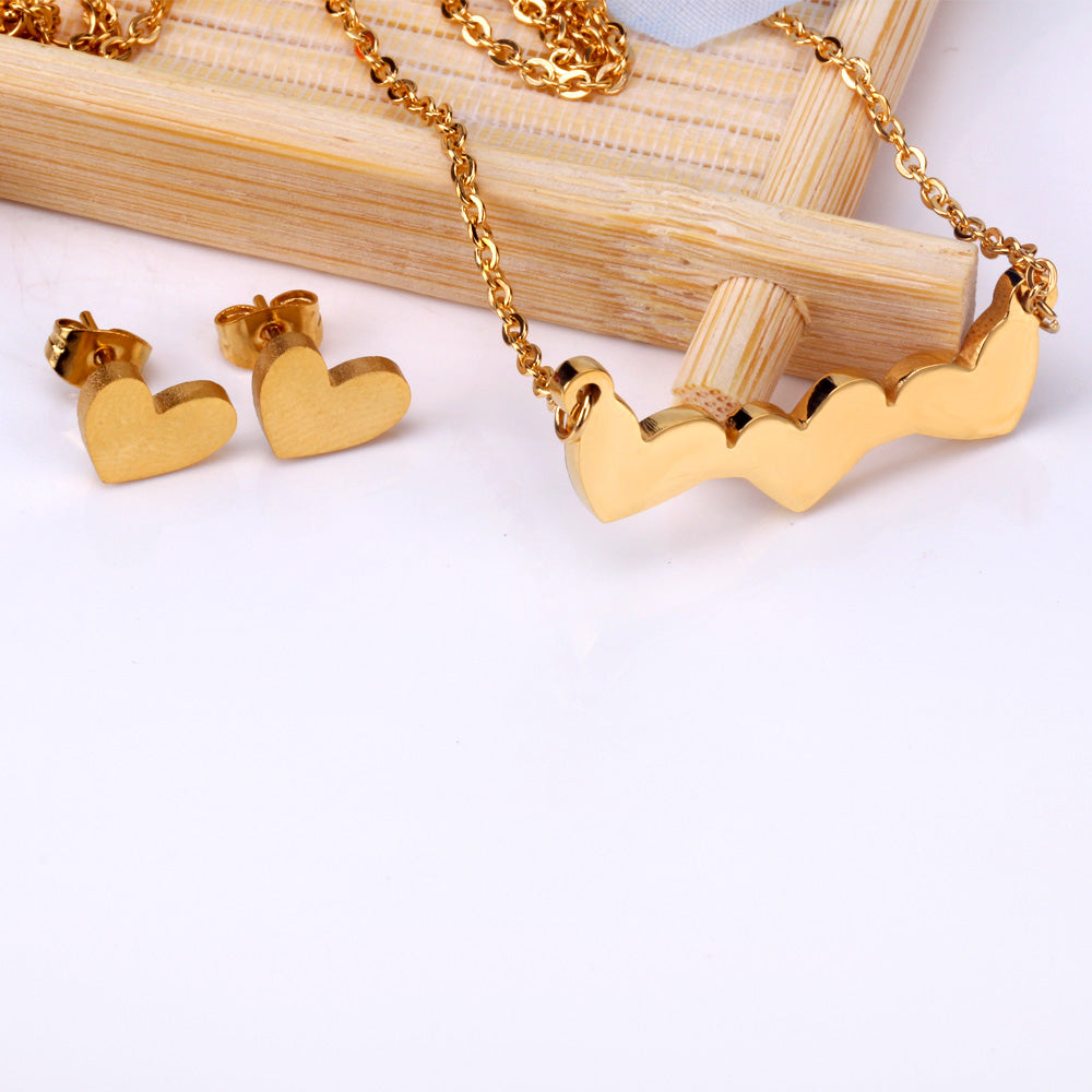 18k gold plated heart-shaped jewelry set including necklace, earrings, and pendant on a light wooden surface.18K Gold Plated on premium Stainless Steel, this necklace and earring set is 100% waterproof, sweat-proof, and anti-tarnish. Designed for active women. Skin-friendly for the Chennai gym heat. Buy 2 Get 1 FREE!