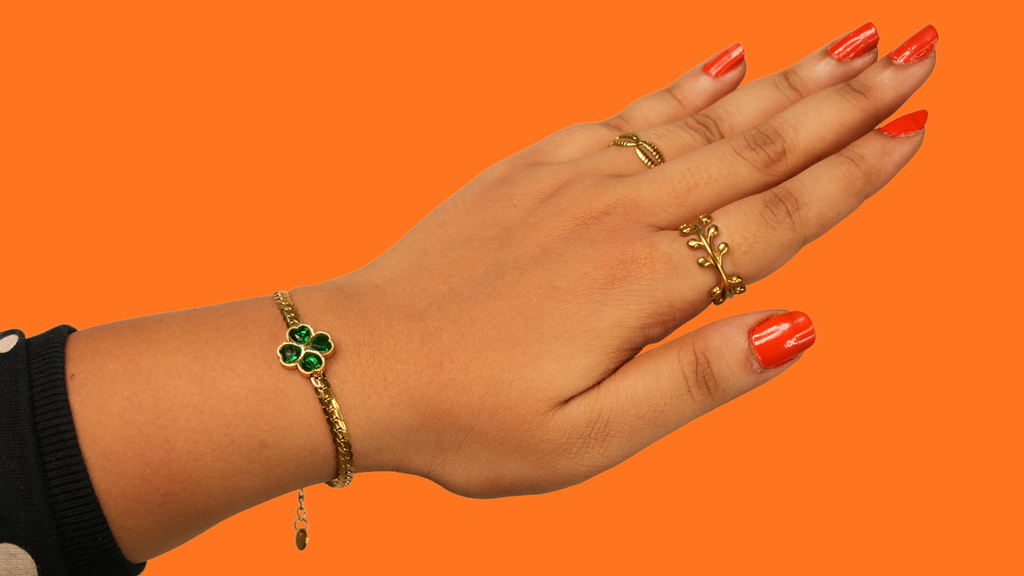 Hand wearing gold rings and a bracelet on an orange background