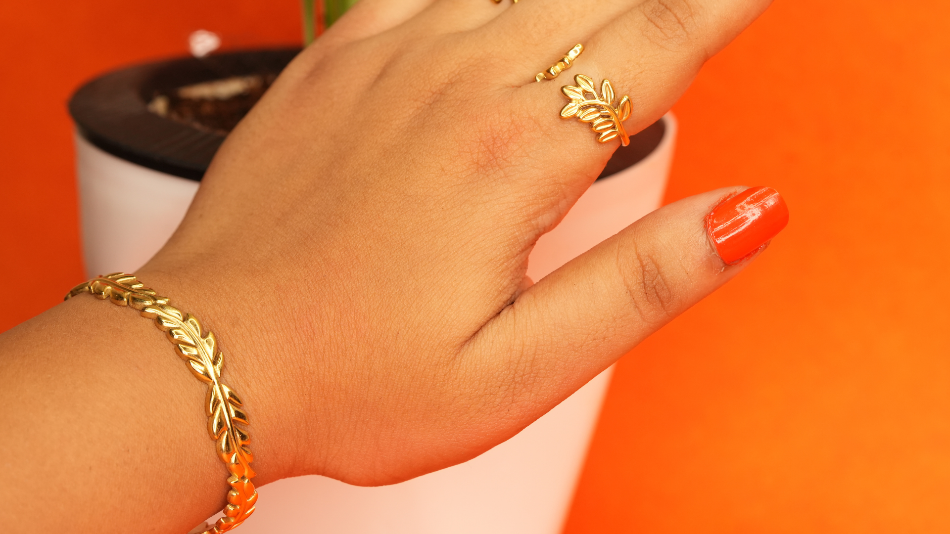Hand wearing a gold bracelet and ring on an orange background